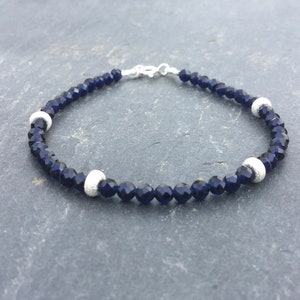 Peut inclure: Un bracelet en cristal bleu foncé avec des accents argentés. Le bracelet est composé de petites perles facettées et possède un fermoir argenté.
