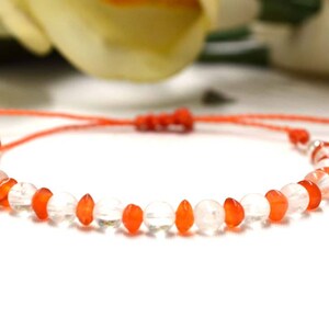 Könnte beinhalten: Ein rotes Armband mit abwechselnd klaren und orangefarbenen Perlen. Das Armband ist mit einem verschiebbaren Knoten verstellbar.