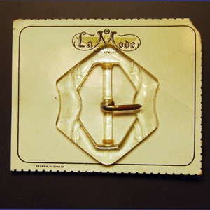 May include: A clear plastic buckle with a metal clasp. The buckle is on a card with the text "La Mode" and "Czecho-Slovakia".