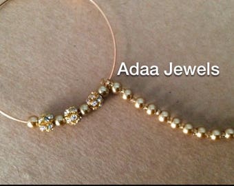 May include: Gold-toned nose ring with a circular design and a beaded chain. The nose ring features sparkling accents and the text "Adaa Jewels".