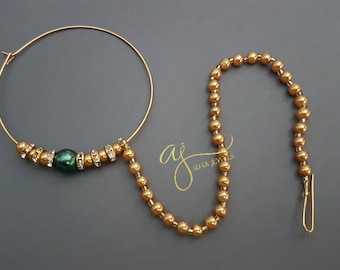 May include: Gold nose ring with a green bead and a chain of gold beads. The chain has a small hook at the end. The nose ring is a traditional Indian jewelry piece.