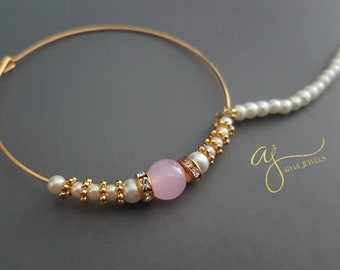 May include: A gold nose ring with a pink stone and white pearls. The ring is attached to a long chain of white pearls.