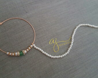 May include: A gold nose ring with a green stone and a pearl chain attached. The chain is made of small white pearls and ends with a small hook.