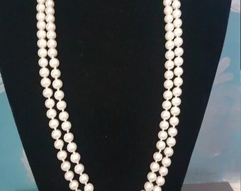 May include: A double strand pearl necklace on a black velvet display stand. The pearls are white and round.