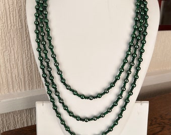 May include: A multi-strand necklace made of dark green glass beads. The necklace is displayed on a white mannequin bust.