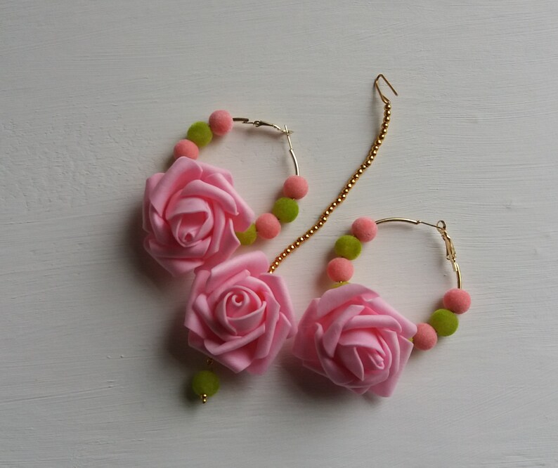 May include: A pair of gold hoop earrings with pink fabric rose accents and green and pink beads.