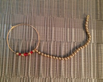 May include: A gold nose ring with a small circle and a chain of gold beads ending in a red gemstone.