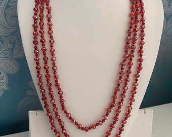 May include: A multi-strand necklace made of red faceted glass beads. The necklace is layered and hangs to the chest.