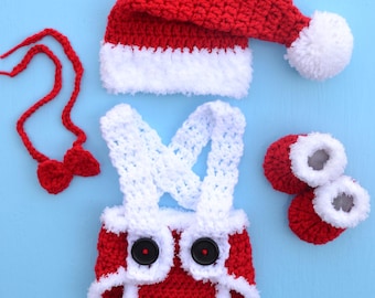May include: A red and white crocheted Santa Claus outfit for a baby. The outfit includes a hat, a diaper cover, booties, and a bow tie.