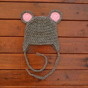 May include: Gray crocheted hat with pink ears, resembling a mouse. The hat has long ties that can be tied under the chin.