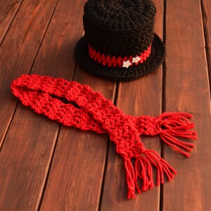 May include: A black crocheted top hat with a red and white trim and a red crocheted scarf with fringe.