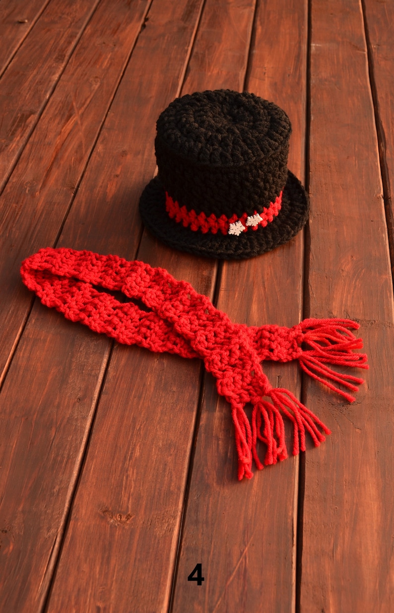 May include: A black crocheted top hat with a red and white trim and a red crocheted scarf with fringe.