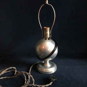 May include: A silver and black globe table lamp with a brass shade and a black cord. The lamp is on a dark blue surface.