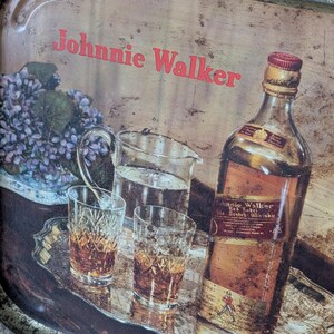 May include: Vintage metal tray with the text "Johnnie Walker" in red. The tray features a bottle of Johnnie Walker Red Label Scotch Whisky, two glasses of amber liquid, a pitcher of water, and a small bouquet of purple flowers.