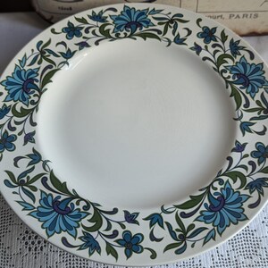 May include: A white ceramic plate with a blue and green floral pattern. The plate has a wide rim and a centre well.