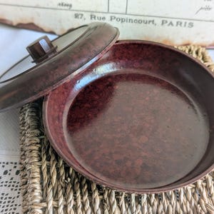 Peut inclure: Un plat en bak&eacute;lite brun avec un couvercle. Le plat est de couleur brun marbr&eacute; et a une finition lisse et brillante. Le couvercle a un petit bouton sur le dessus.