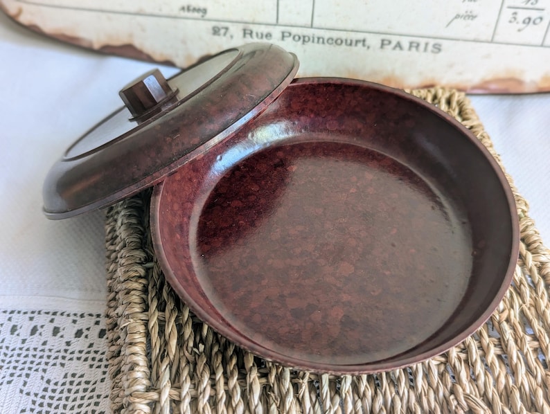 Peut inclure: Un plat en bak&eacute;lite brun avec un couvercle. Le plat est de couleur brun marbr&eacute; et a une finition lisse et brillante. Le couvercle a un petit bouton sur le dessus.