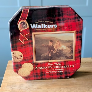 Może przedstawiać: Czerwono-czarne pudełko w kratę z Walkers Assorted Shortbread. Pudełko zawiera obraz dzieci i tekst "Pure Butter Assorted Shortbread". Pudełko zawiera 500g ciasteczek maślanych.