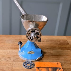 May include: Vintage Spong 601 mincer, a manual meat grinder. The mincer is blue and silver, with a wooden handle. Includes a metal grinding plate and an orange instruction sheet with the text "SPONG 601 MINCER".