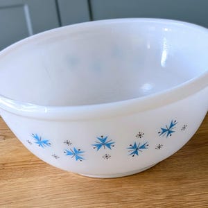 May include: White mixing bowl with a rounded shape and a blue and black starburst pattern. The bowl is made of a smooth, opaque material and is suitable for kitchen use.