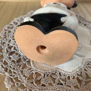 May include: A vintage Mickey Mouse figurine, viewed from the bottom up, showcasing the character's iconic black shorts and large, tan feet. The figurine is made of a light-colored material, with the words "Disney Prod." and "Made in Japan" visible on the sole.