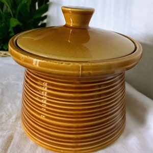 May include: A brown ceramic jar with a lid. The jar has a ribbed design and a glossy finish.