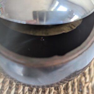 Peut inclure: Un pot en c&eacute;ramique brun fonc&eacute; avec un couvercle argent&eacute;. Le couvercle est l&eacute;g&egrave;rement entrouvert, r&eacute;v&eacute;lant l'int&eacute;rieur du pot.
