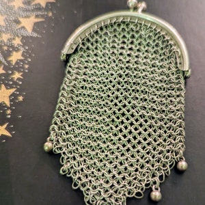 Puede incluir: Una cartera de malla de cadena plateada con una parte superior con bisagras y una franja de cuentas decorativas.