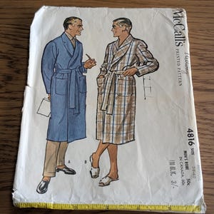May include: A McCall's printed pattern envelope for a robe, size medium 38-40, featuring illustrations of two robe styles. A yellow measuring tape is placed along the bottom edge, showing a length of approximately 23 cm across the paper envelope.