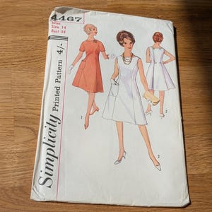 May include: A Simplicity 4467 sewing pattern envelope for a dress in size 14, bust 34. The white paper envelope features illustrations of three variations of a sleeveless or short-sleeved A-line dress with pockets, shown in orange and white.