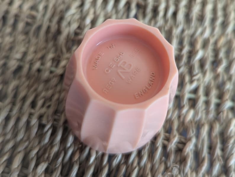 Peut inclure: Un bouchon de bouteille en plastique rose avec le texte "REGD. CE648 NP WARE MADE IN ENGLAND" sur le dessus.