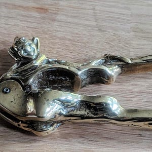 May include: A brass nutcracker in the shape of a whimsical creature with a detailed design. The nutcracker is open, revealing the mechanism for cracking nuts.