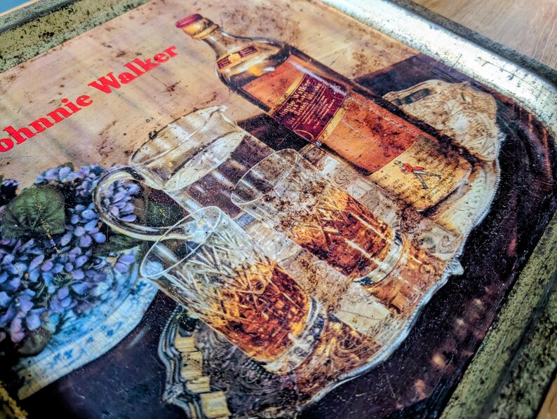 May include: Vintage metal serving tray with a whiskey bottle, glasses, and a floral arrangement. The tray features the text "Johnnie Walker" in red. The image has a warm, aged aesthetic.