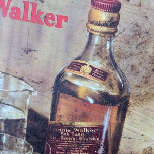 May include: Vintage Johnnie Walker Red Label Scotch Whisky bottle with a red and gold label. The bottle has a red cap and is partially visible with the word "Walker" in red above it. The image has a rustic, aged appearance.
