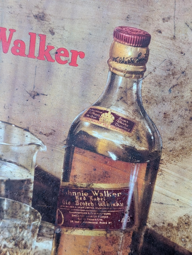 May include: Vintage Johnnie Walker Red Label Scotch Whisky bottle with a red and gold label. The bottle has a red cap and is partially visible with the word "Walker" in red above it. The image has a rustic, aged appearance.