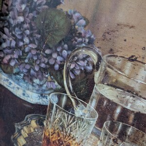 May include: A vintage serving tray with a floral arrangement of purple flowers in a blue and white vase, and several crystal glasses filled with amber liquid. A pitcher of water is also visible.