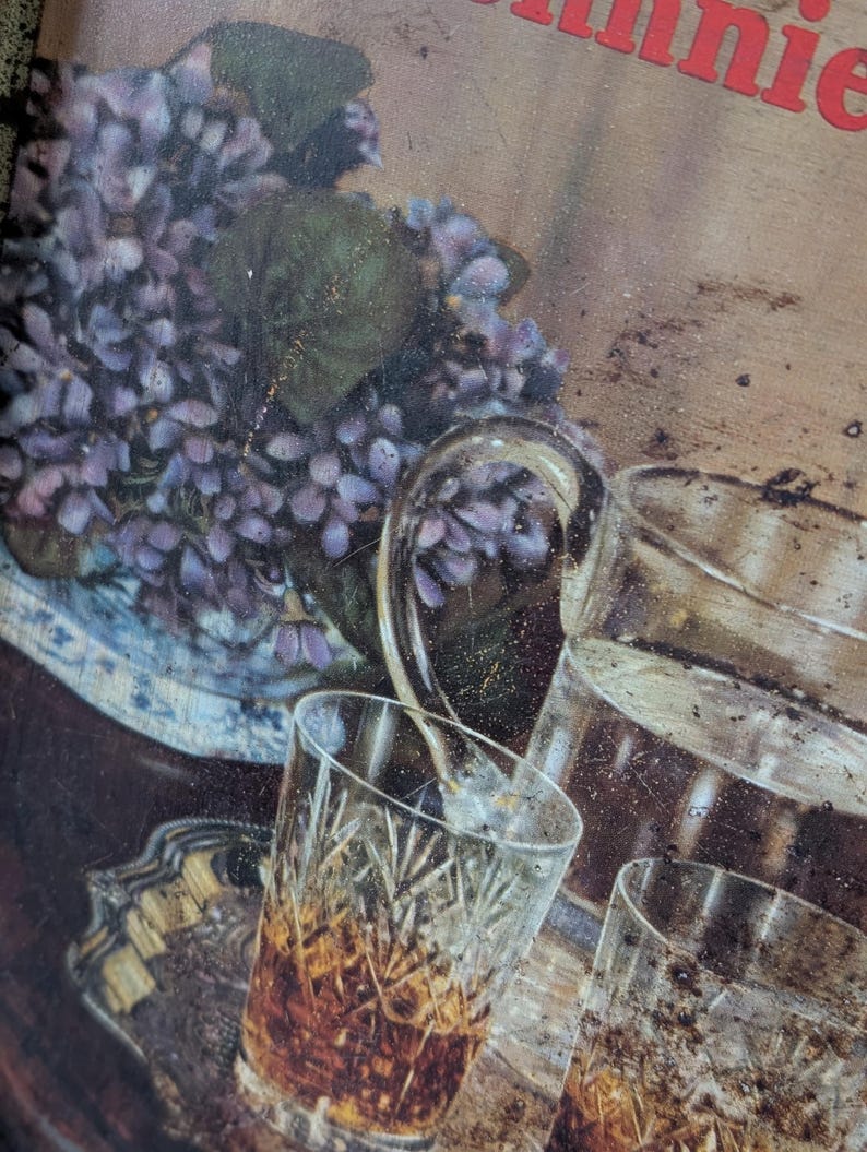 May include: A vintage serving tray with a floral arrangement of purple flowers in a blue and white vase, and several crystal glasses filled with amber liquid. A pitcher of water is also visible.