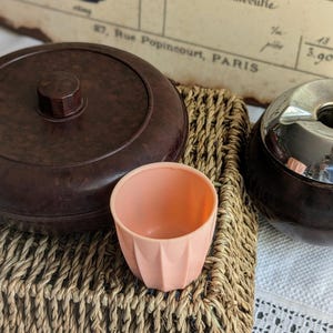 Puede incluir: Un juego de tres recipientes vintage de baquelita marrón y negro con tapa plateada. Los recipientes están sobre una cesta tejida.