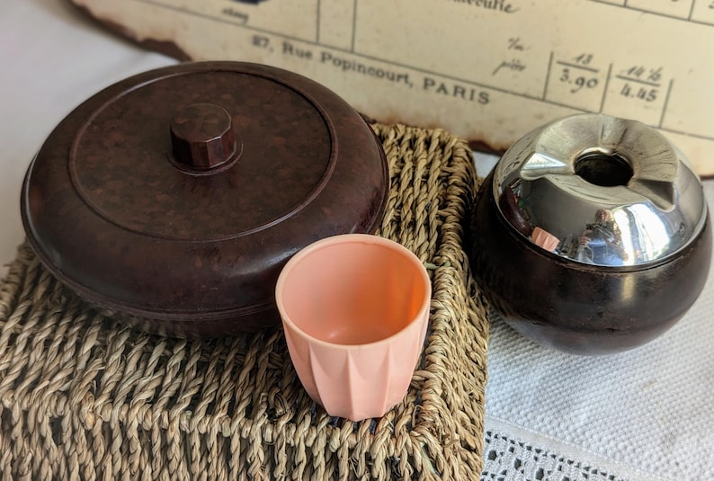 Peut inclure: Ensemble de trois contenants vintage en bak&eacute;lite brun et noir avec un couvercle argent&eacute;. Les contenants sont pos&eacute;s sur un panier en osier.