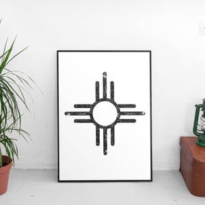 Pode incluir: Uma impress&atilde;o em preto e branco do s&iacute;mbolo Zia, um desenho tradicional nativo americano, em uma moldura preta em uma parede branca.