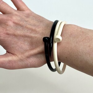 May include: Two bangle bracelets, one black and one white, with a nail-shaped design. The bracelets are worn on a person's wrist.