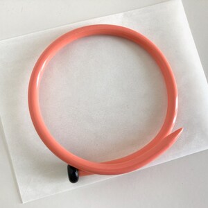 May include: A coral-colored plastic headband with a black nail-shaped accent at the end.