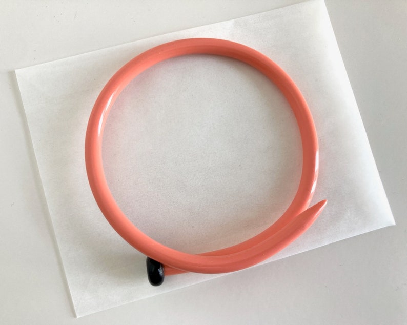 May include: A coral-colored plastic headband with a black nail-shaped accent at the end.