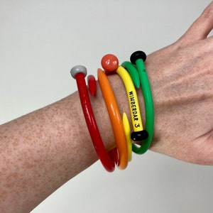 May include: A set of five colorful plastic bracelets with a black and white label that reads "WIMBERDAR 3".