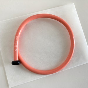 May include: A pink plastic knitting needle with a black tip and the text "DUREX 5" printed on the side.
