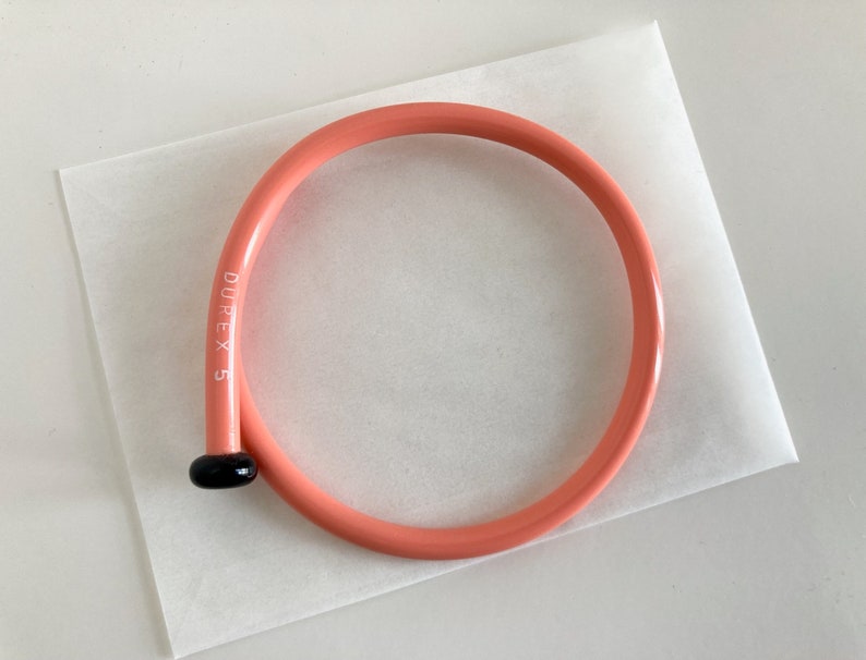 May include: A pink plastic knitting needle with a black tip and the text "DUREX 5" printed on the side.