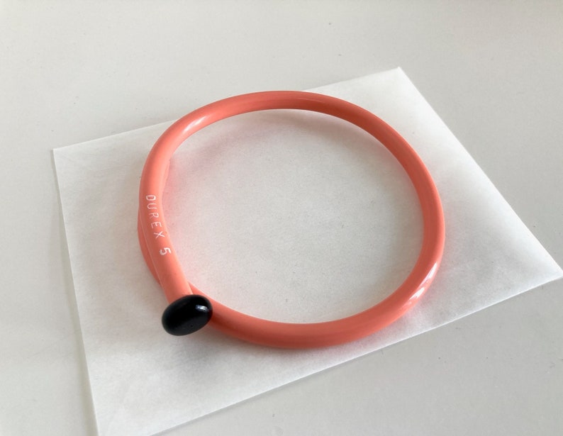 May include: A pink plastic headband with the text "DUPEX 5" printed on the side. The headband has a black plastic accent on the side.