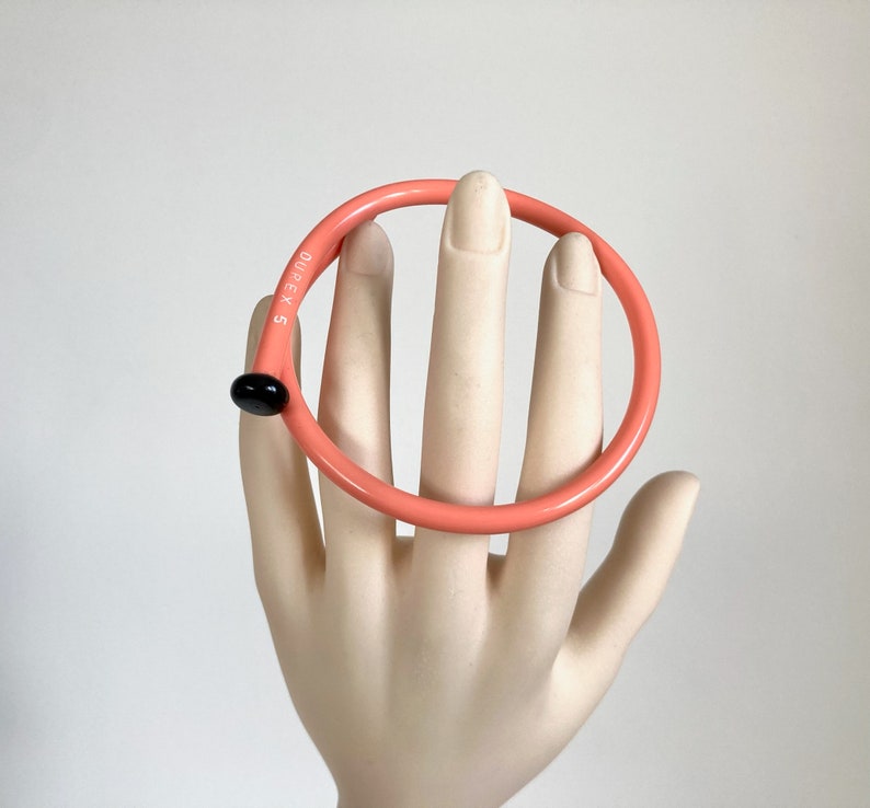 May include: A pink plastic bangle with a black dot and the text "DUREX 5" on the side.