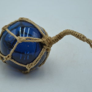 May include: A blue glass fishing float with a natural twine net. The float has a long twine rope attached to it.