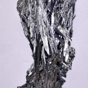Pode incluir: Um espécime mineral impressionante, com aspeto metálico e estrutura cristalina complexa. O mineral é predominantemente de cor cinza prateado escuro, com áreas de alta refletividade. A forma geral é irregular, com numerosos cristais afiados e alongados.